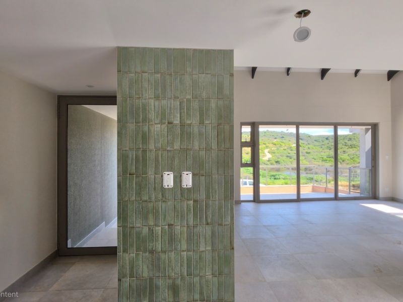 Spacious open-plan living area featuring a striking green tiled feature wall, large sliding doors with scenic views, and modern neutral floor tiles.