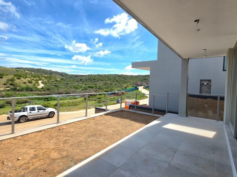 Spacious unfinished balcony featuring tiled flooring, glass balustrades, and scenic landscape views, requiring final finishes and landscaping to complete the outdoor living space.