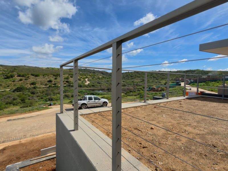 An elevated outdoor terrace featuring a modern stainless steel cable railing system, overlooking a natural landscape and driveway area.