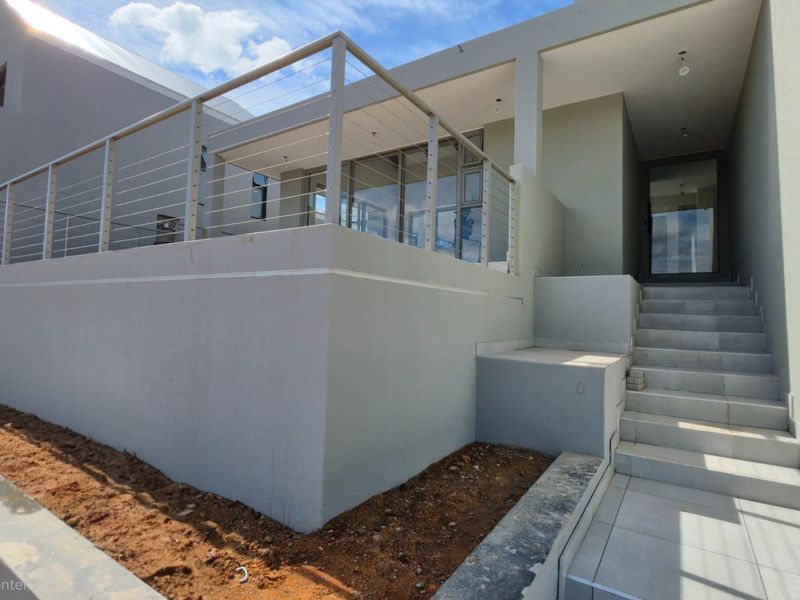 Modern rear exterior featuring a raised patio with stainless steel cable railings, tiled stairs, and glass sliding doors, currently awaiting final landscaping.