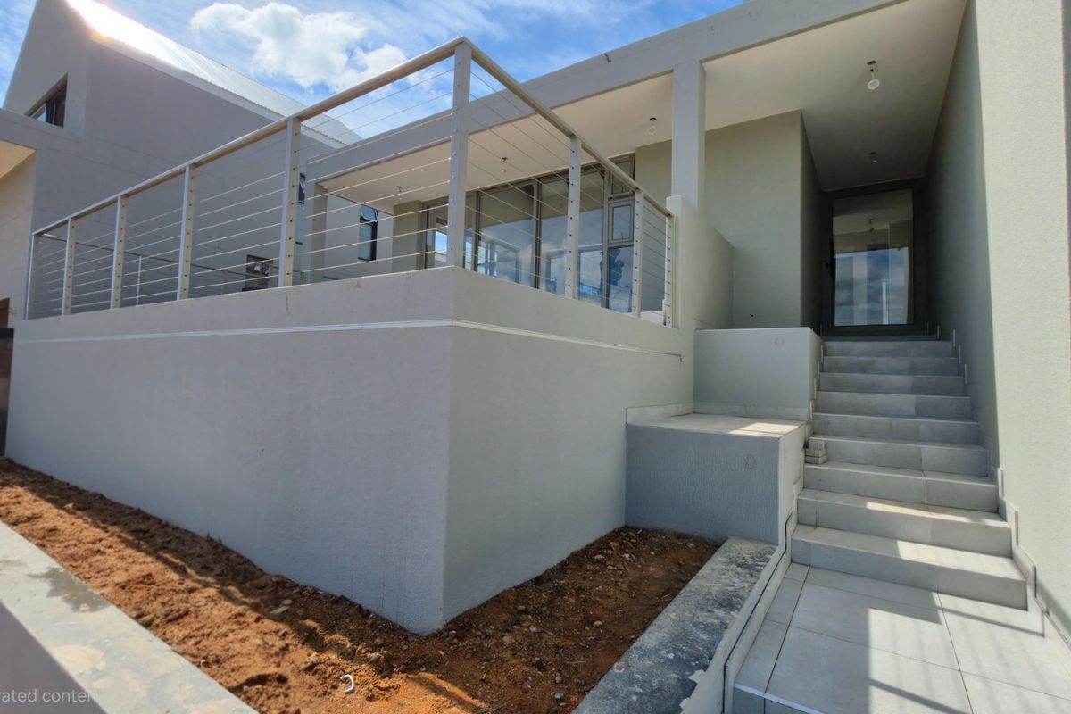 Modern rear exterior featuring a raised patio with stainless steel cable railings, tiled stairs, and glass sliding doors, currently awaiting final landscaping.