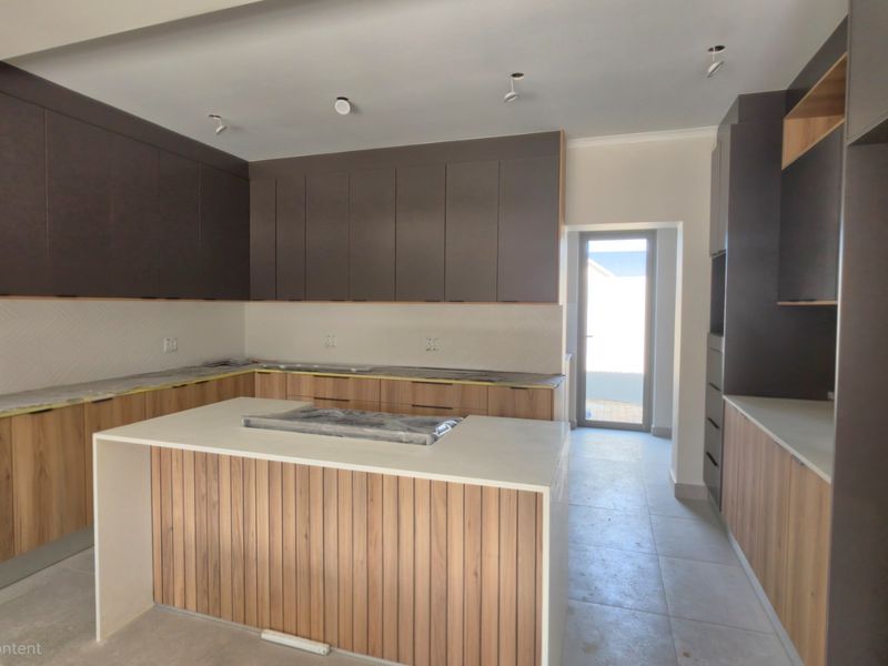 A modern, newly installed kitchen featuring a central island, two-tone cabinetry, stone countertops, and a tiled backsplash, currently in a pristine, unfinished state.