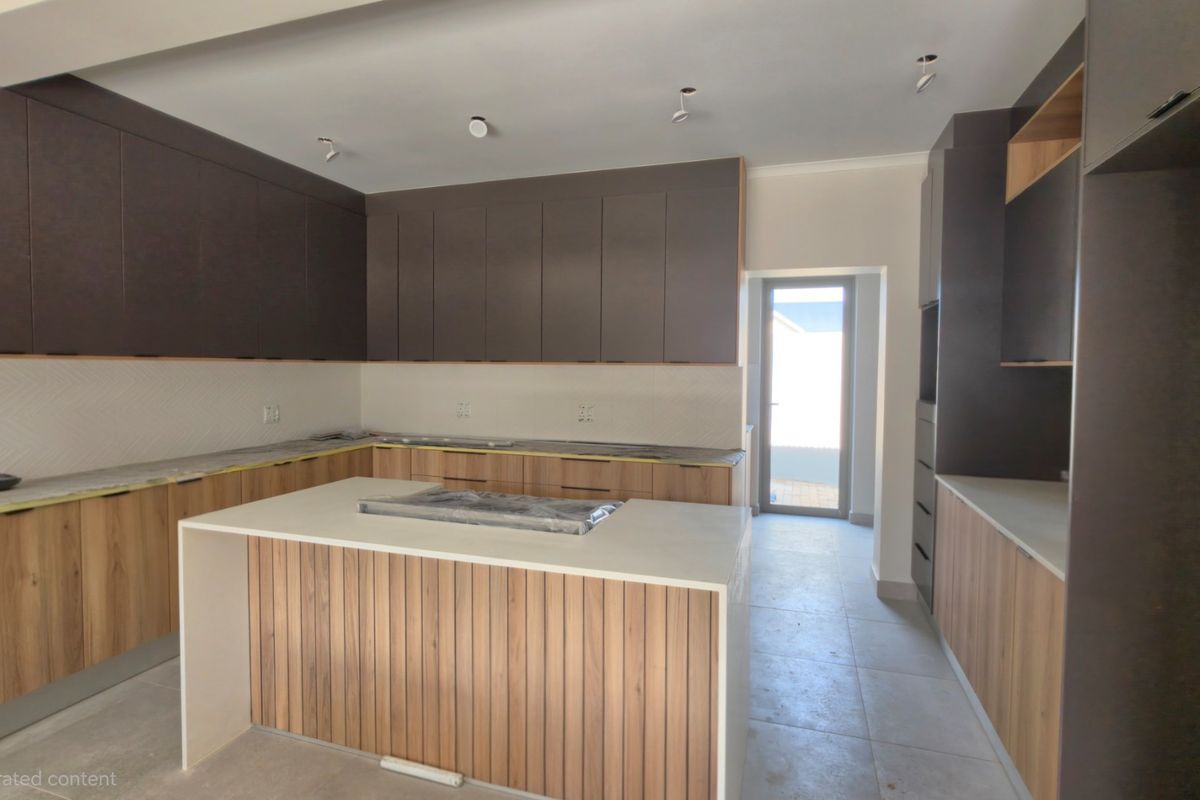 A modern, newly installed kitchen featuring a central island, two-tone cabinetry, stone countertops, and a tiled backsplash, currently in a pristine, unfinished state.
