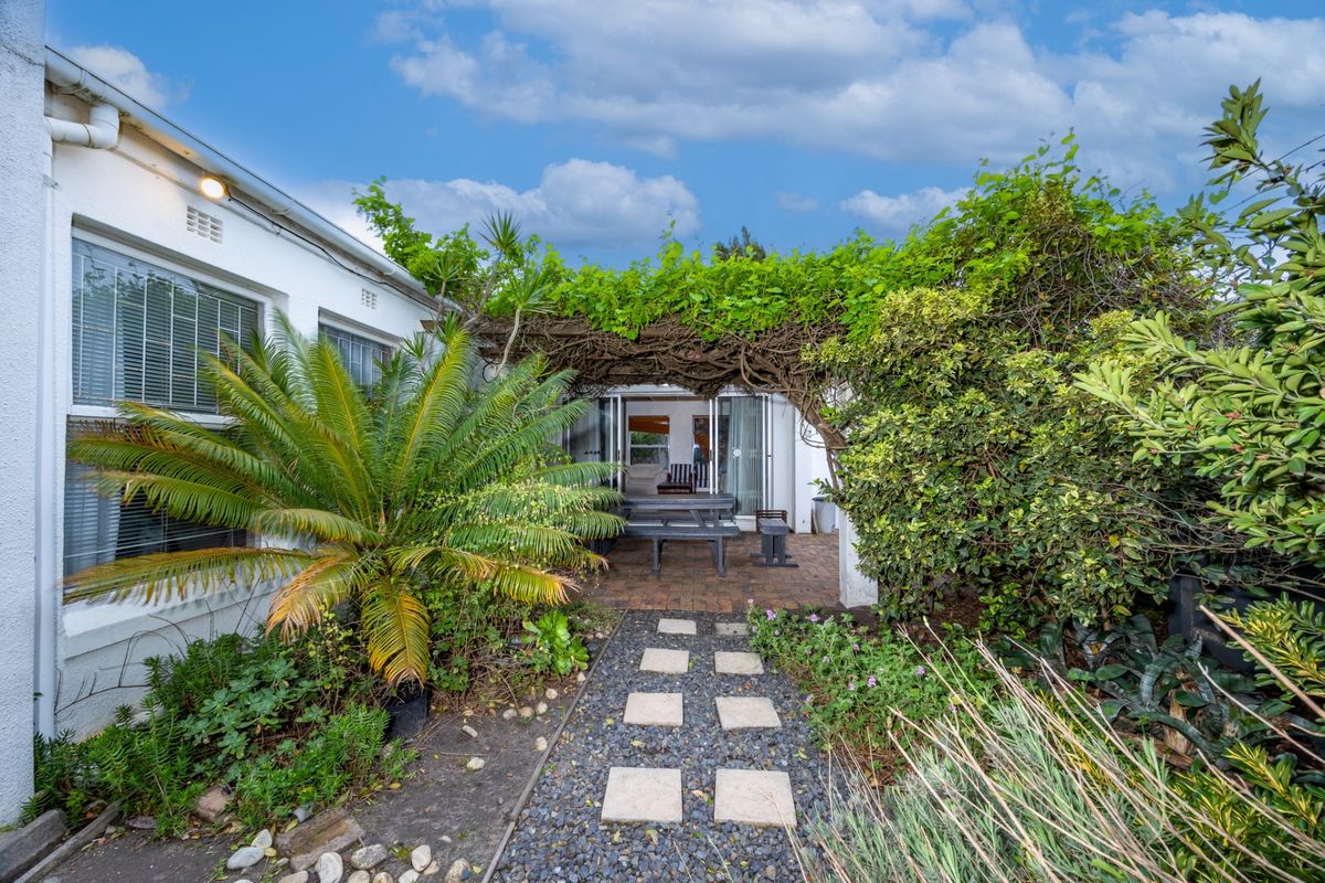 A rear garden patio area featuring a vine-covered pergola, brick paving, and direct access to the home through sliding glass doors.