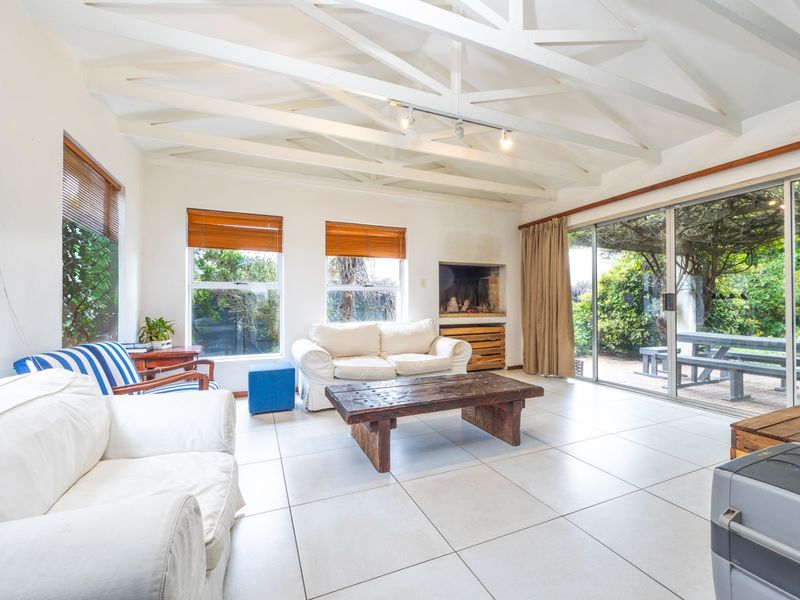 Spacious living room featuring exposed white timber ceiling beams, large tiled flooring, a built-in fireplace, and sliding glass doors opening to the garden.