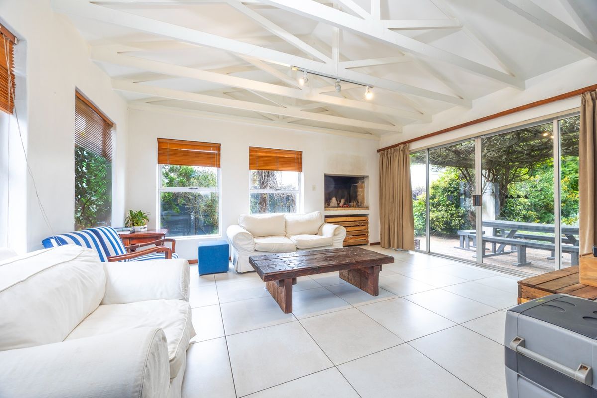 Spacious living room featuring exposed white timber ceiling beams, large tiled flooring, a built-in fireplace, and sliding glass doors opening to the garden.