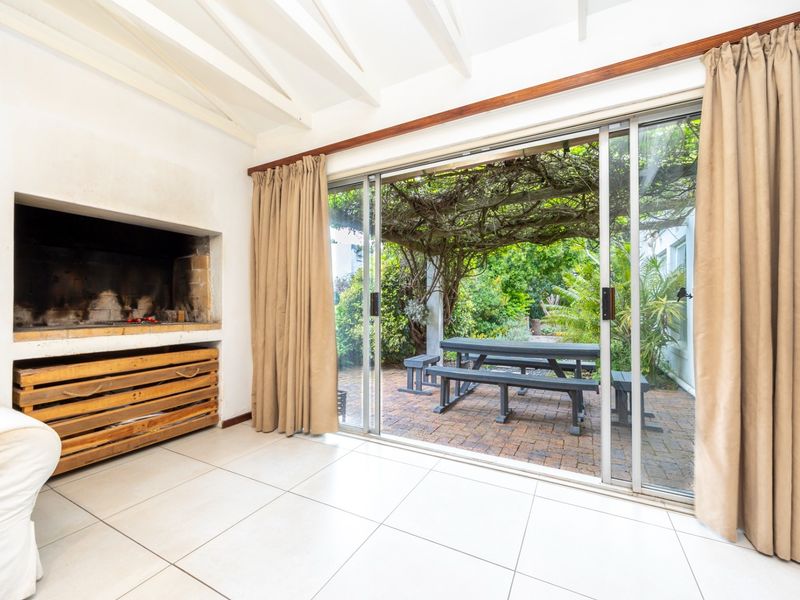 Indoor entertainment area featuring a built-in fireplace, exposed beam ceiling, and large sliding glass doors opening onto a paved patio garden.