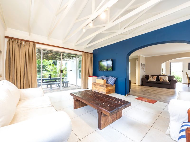 Spacious living room featuring exposed white timber rafters, tiled flooring, a feature blue wall, and large sliding doors providing access to the outdoor area.