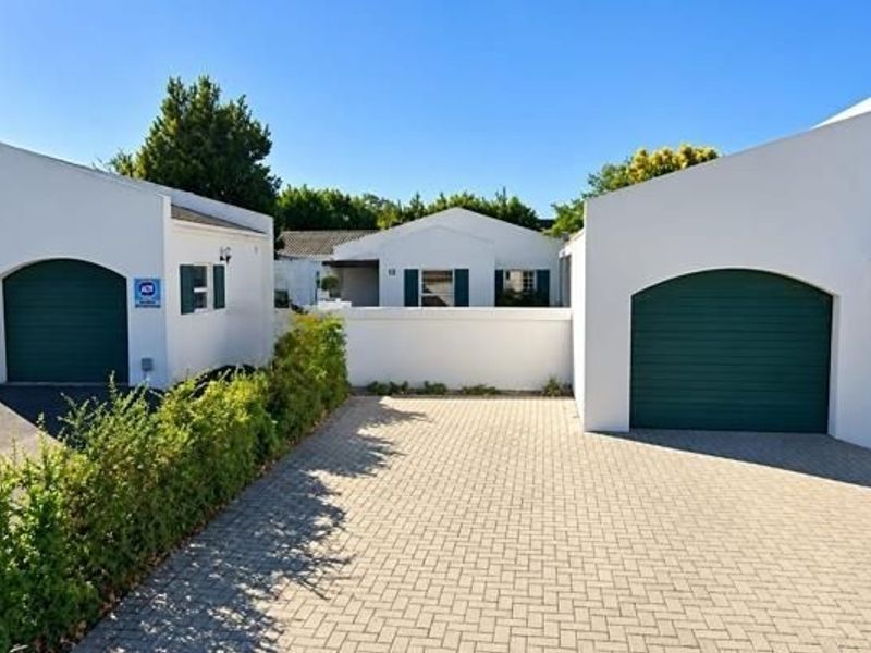 Front view of the property featuring a paved driveway, two separate garages with green doors, and a white boundary wall.