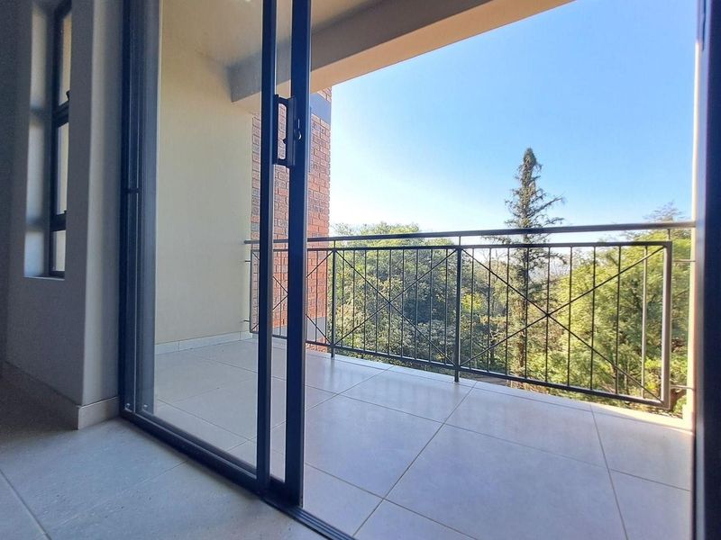 A clean, tiled balcony featuring a metal balustrade and sliding glass door access, offering a pleasant view of the surrounding trees.