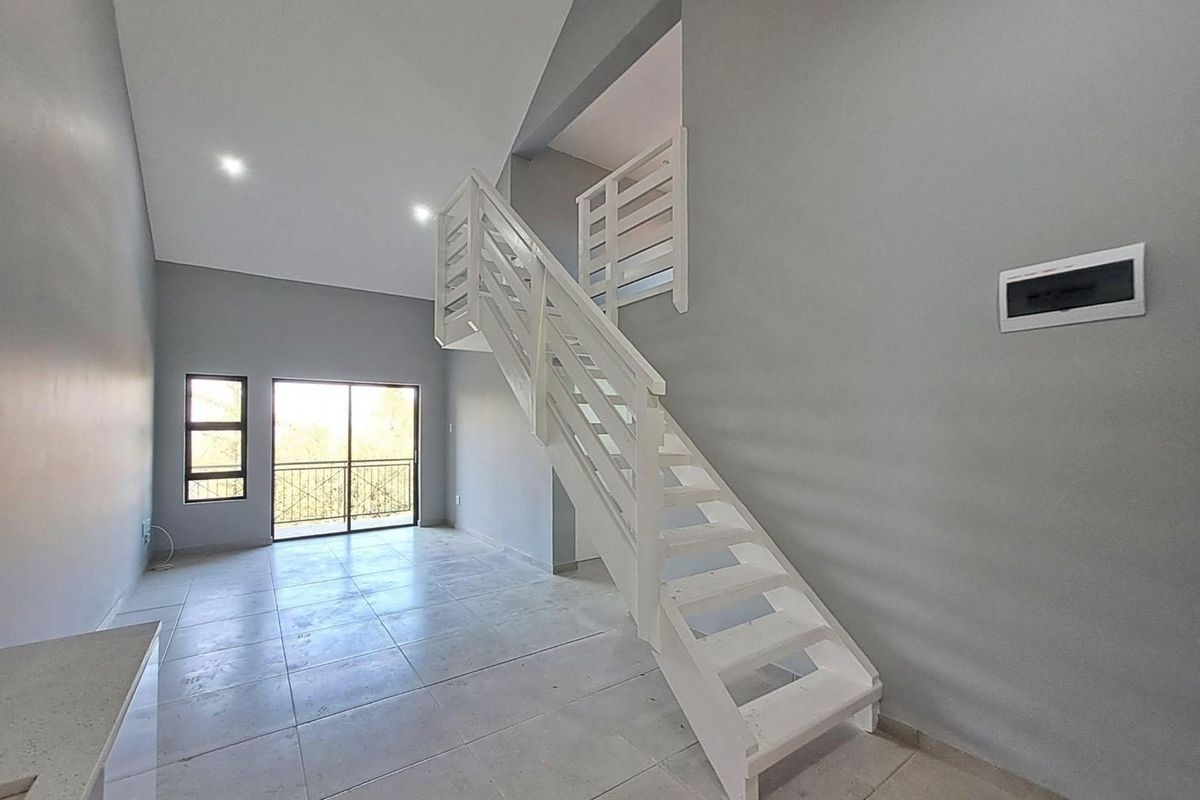 Spacious open-plan living area featuring high ceilings, tiled flooring, a modern staircase, and direct access to a balcony.