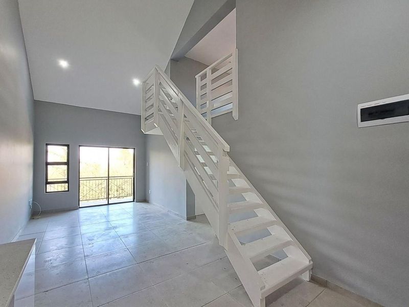 Spacious open-plan living area featuring high ceilings, tiled flooring, a modern staircase, and direct access to a balcony.