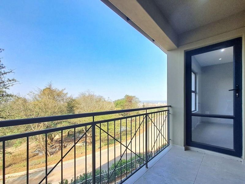 A clean, modern balcony featuring tiled flooring, a secure metal balustrade, and a glass door leading into the apartment with scenic outdoor views.