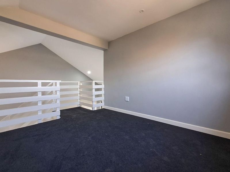 An empty loft-style bedroom featuring dark carpeting, white safety railings, and neutral grey walls with recessed lighting.