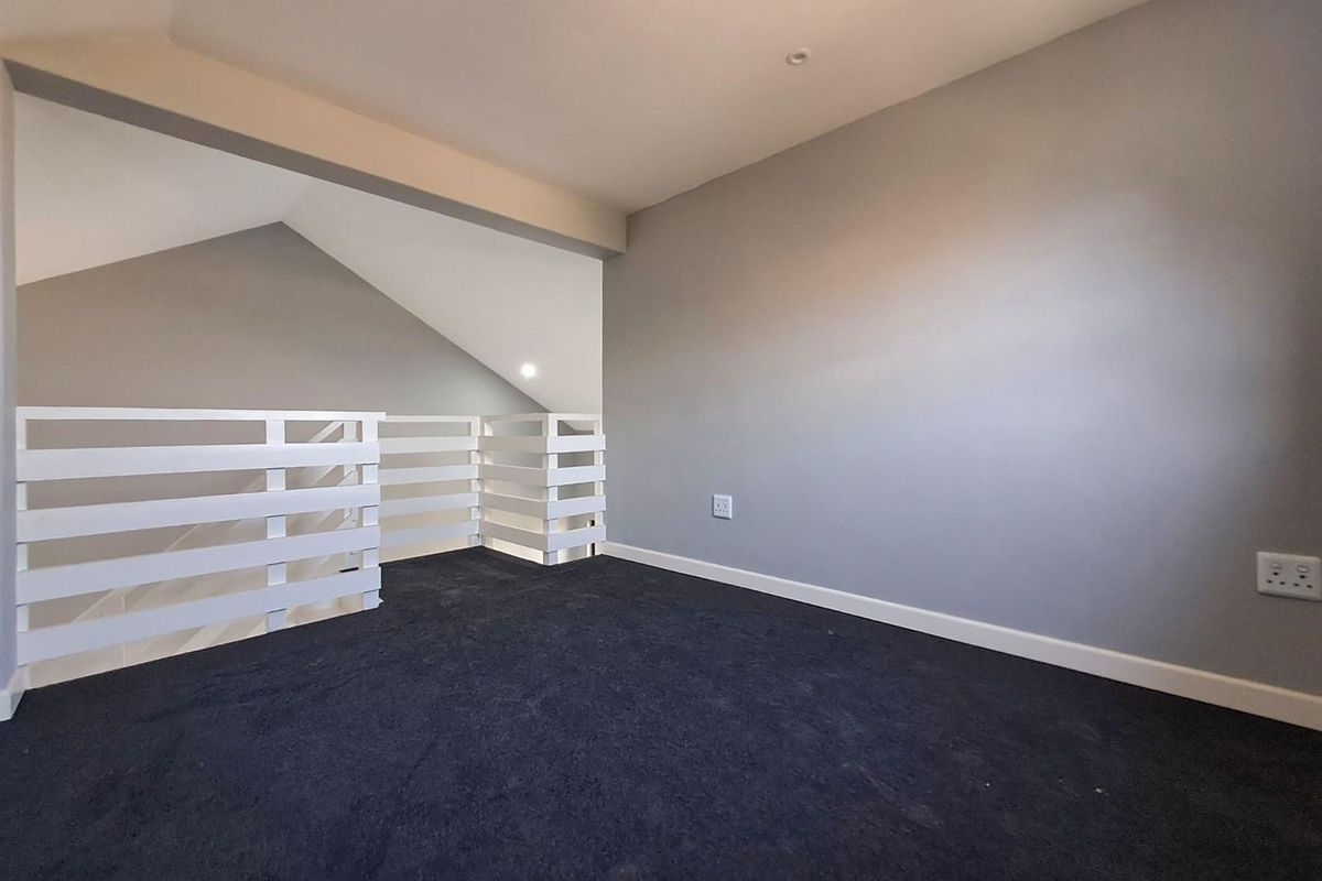 An empty loft-style bedroom featuring dark carpeting, white safety railings, and neutral grey walls with recessed lighting.