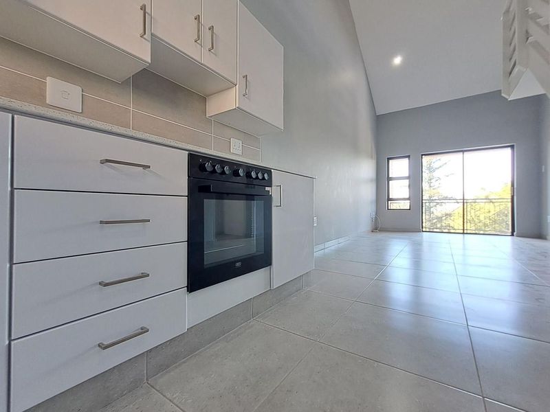 Open-plan kitchen and living area featuring modern white cabinetry, built-in oven, tiled flooring, and access to a balcony through sliding glass doors.