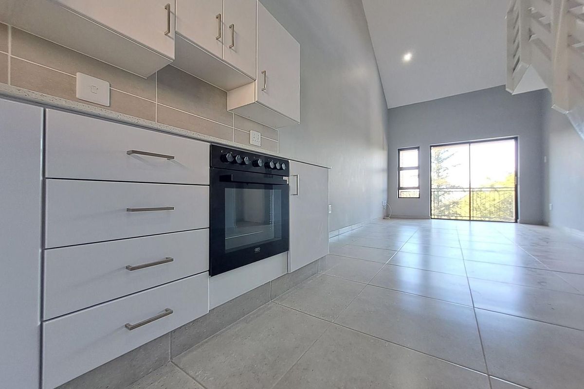 Open-plan kitchen and living area featuring modern white cabinetry, built-in oven, tiled flooring, and access to a balcony through sliding glass doors.