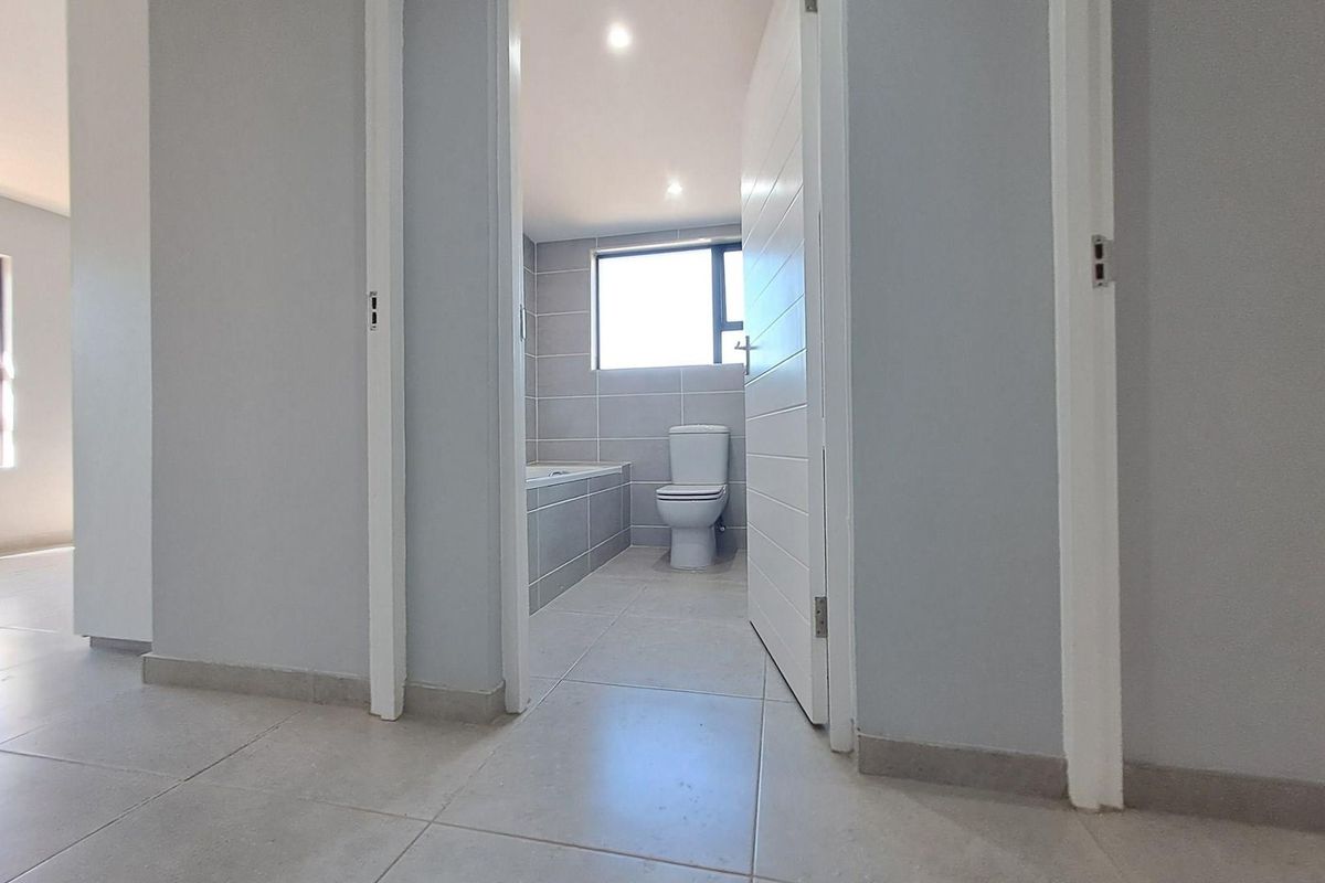 A clean, modern bathroom featuring tiled walls and floors, a built-in bathtub, and a toilet, viewed from the adjacent hallway.