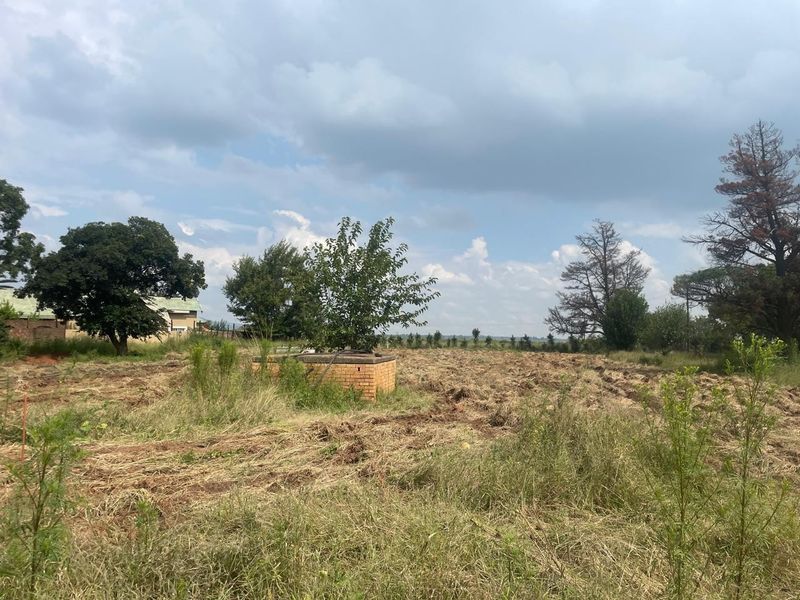 An expansive, undeveloped plot of land featuring natural vegetation and a small brick-built utility structure.