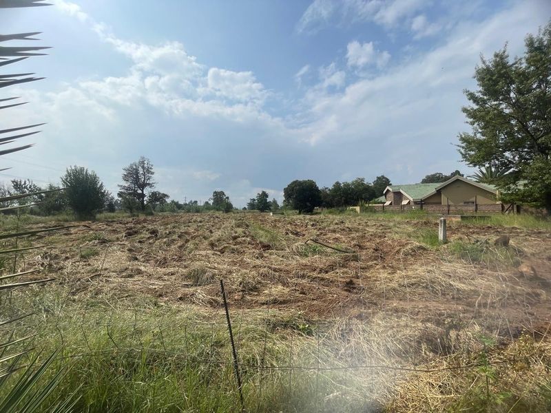 A view of a large, tilled agricultural plot of land enclosed by wire fencing, with a residential building visible in the background.