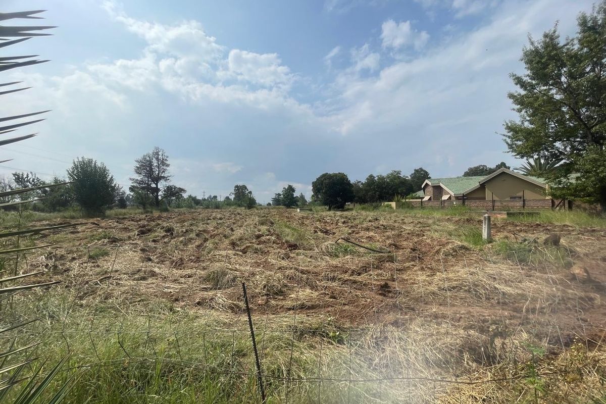 A view of a large, tilled agricultural plot of land enclosed by wire fencing, with a residential building visible in the background.