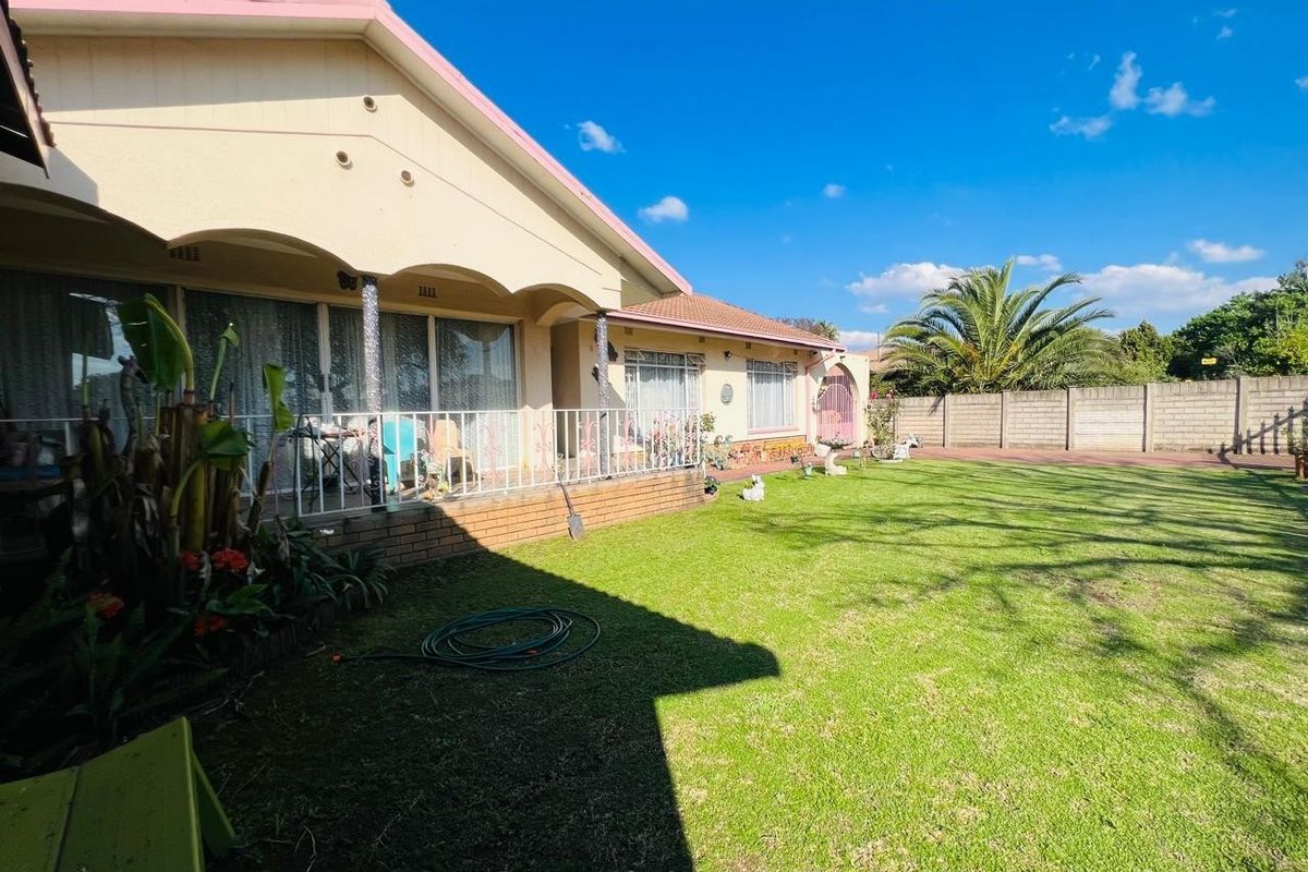 Rear view of the property featuring a covered patio, a spacious lawn, and a secure perimeter wall.
