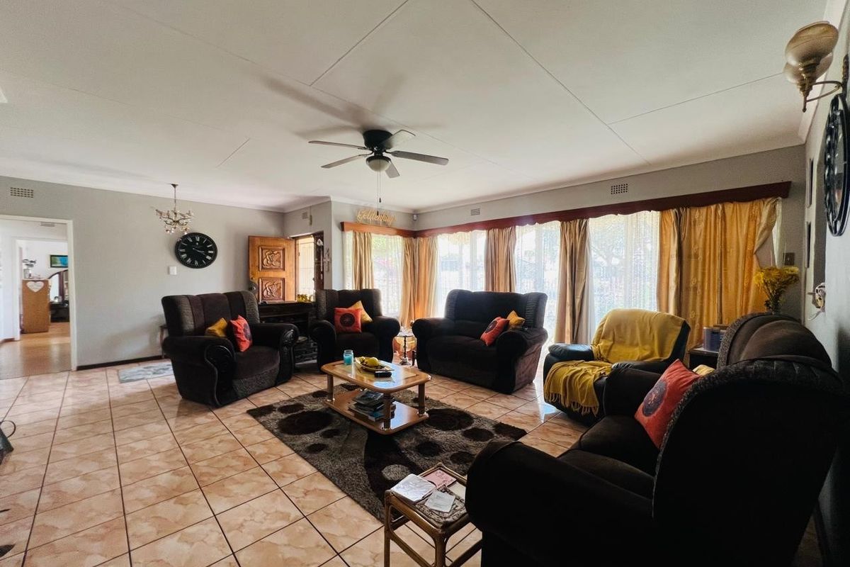 A spacious living room featuring tiled flooring, a ceiling fan, and large windows that allow for natural light.