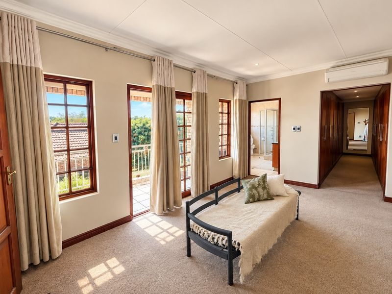 Spacious bedroom featuring built-in cupboards, split-system air conditioning, and direct access to a private balcony through timber-framed glass doors.