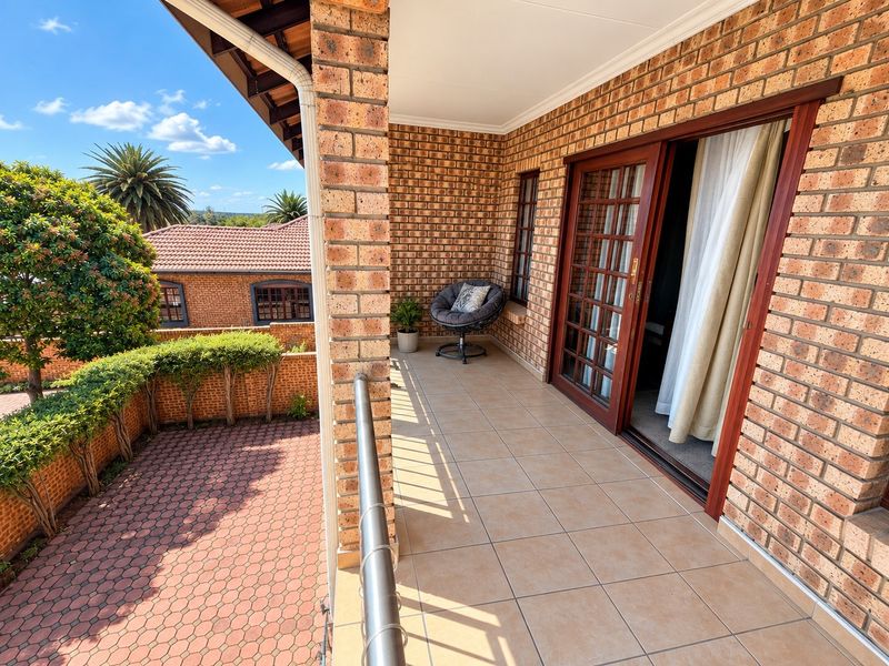 A covered balcony featuring brick walls, tiled flooring, and a metal railing, providing access to the interior through sliding glass doors.