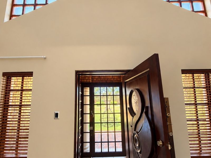 Spacious entrance hall featuring high vaulted ceilings, glass block clerestory windows, tiled flooring, and a decorative timber front door.
