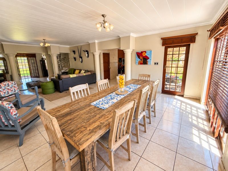 Spacious open-plan dining and living area featuring tiled floors, decorative columns, and direct access to the outdoor patio through timber-framed glass doors.