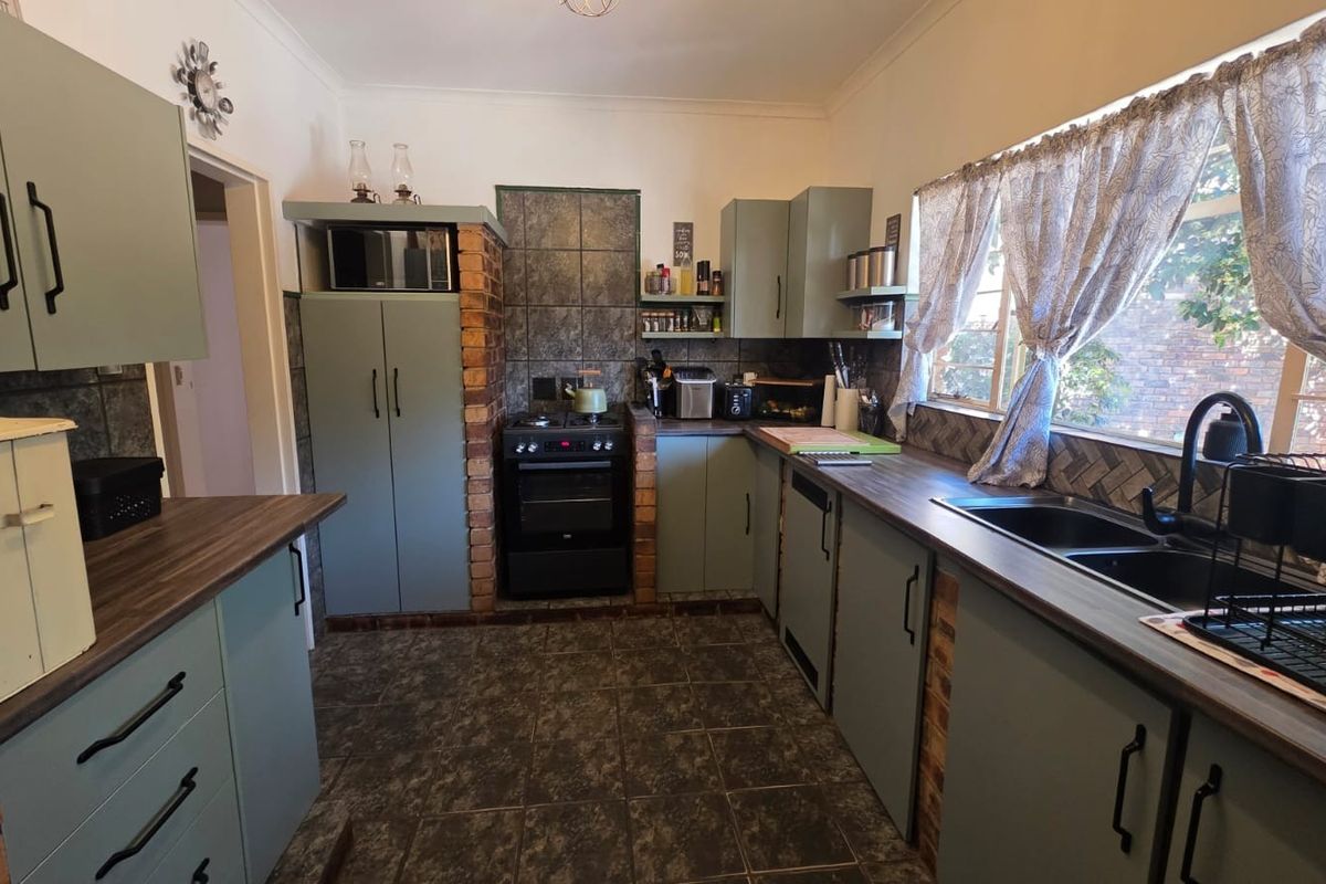 A functional kitchen featuring sage green cabinetry, dark laminate countertops, exposed brick accents, and a tiled splashback with a built-in oven and hob.