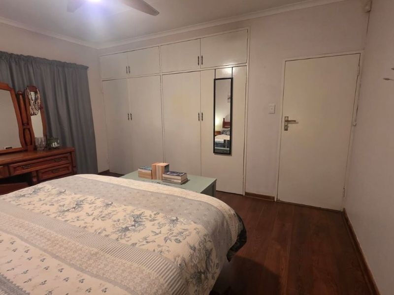 A bedroom featuring laminate flooring, a ceiling fan, and extensive built-in cupboard storage.