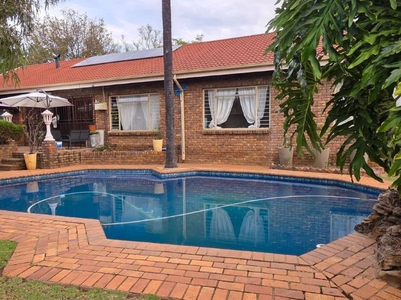 A well-maintained backyard featuring a swimming pool with brick paving, set against a facebrick house with a tiled roof and solar panels.