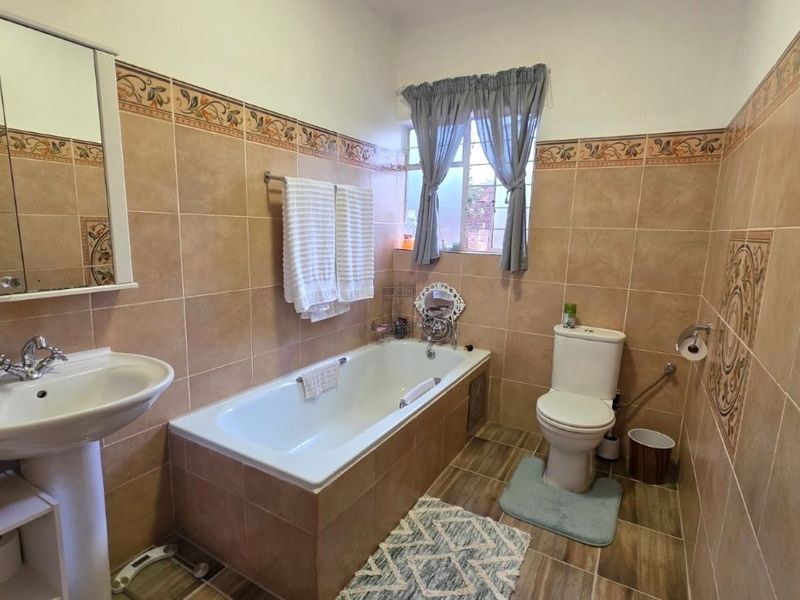 A functional bathroom featuring a pedestal basin, built-in bathtub, and toilet, finished with neutral wall and floor tiling.