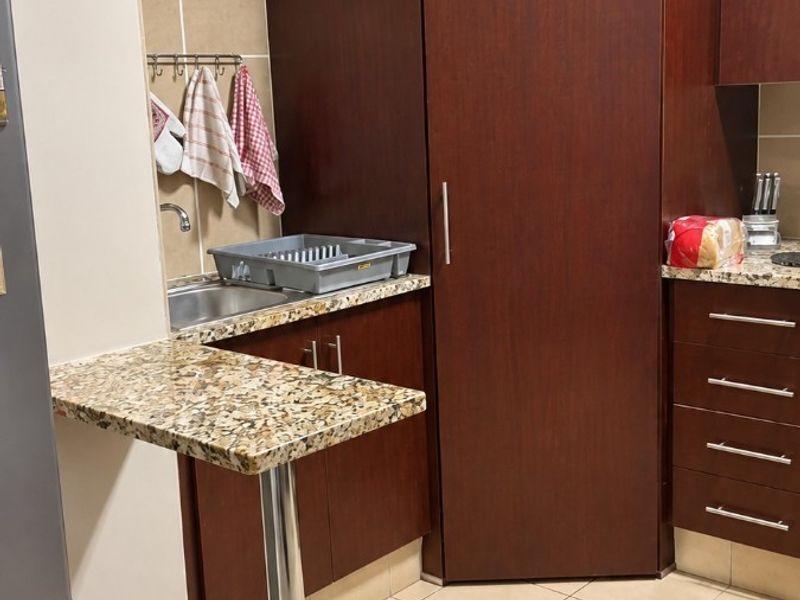 A functional kitchen featuring dark wood cabinetry, granite countertops, a breakfast bar, and tiled flooring with a neutral backsplash.