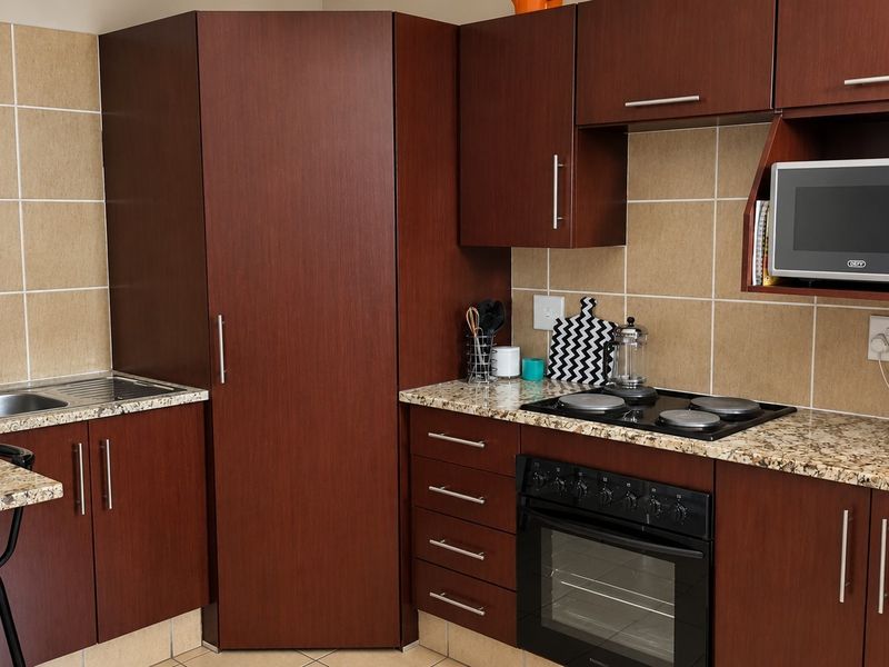 A functional kitchen featuring dark wood cabinetry, granite countertops, a built-in oven with electric hob, and a tiled backsplash.