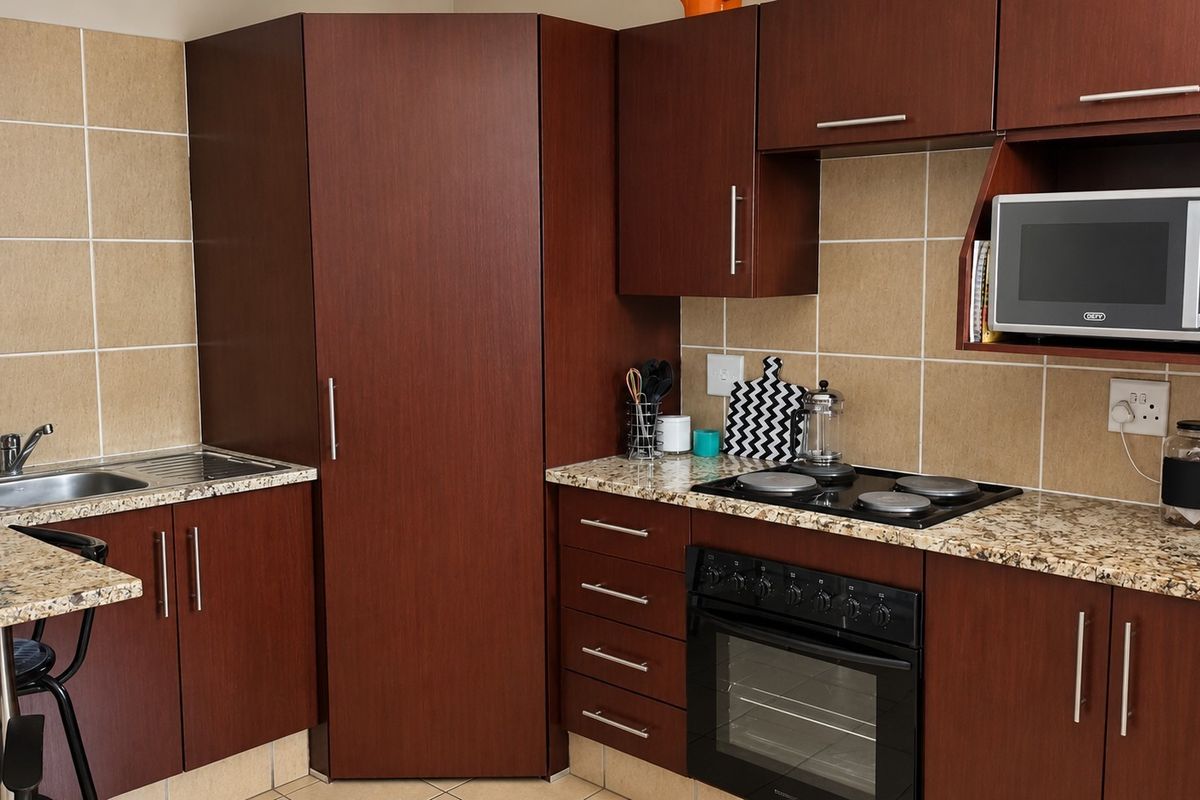 A functional kitchen featuring dark wood cabinetry, granite countertops, a built-in oven with electric hob, and a tiled backsplash.