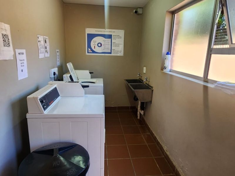 Functional laundry room featuring tiled flooring, a stainless steel double sink, and multiple top-loading washing machines.
