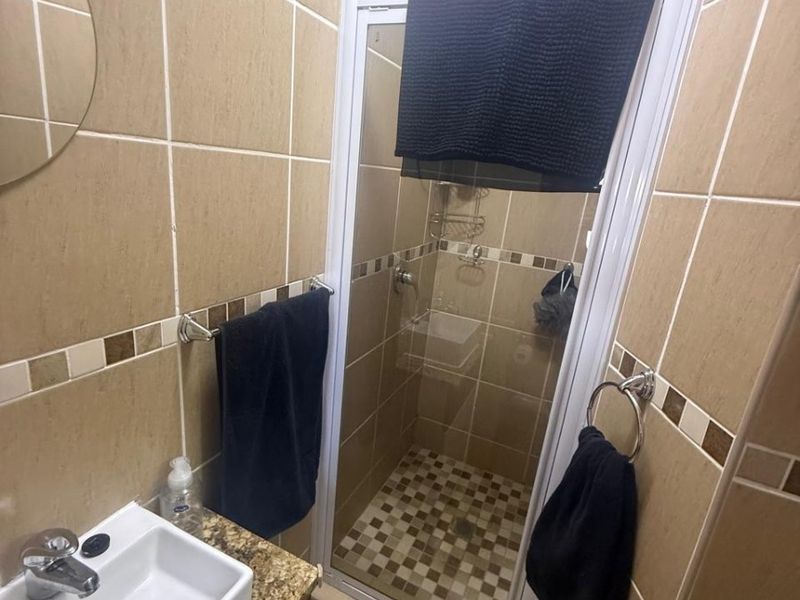 Compact bathroom featuring a shower enclosure, vanity basin with mixer tap, and neutral wall and floor tiling.