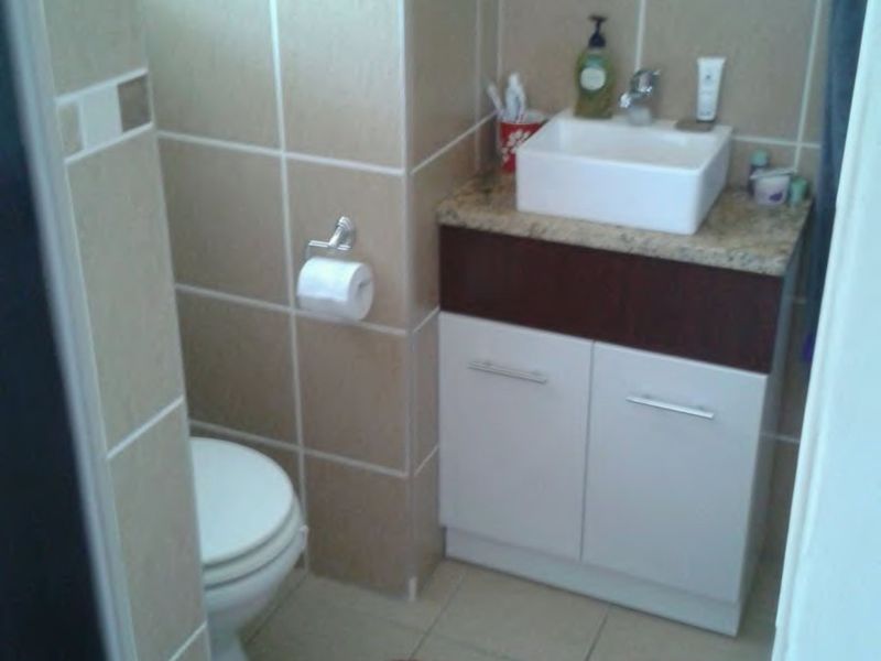Compact bathroom featuring a modern vessel sink on a granite-topped vanity cabinet, neutral wall tiling, and standard toilet fixture.