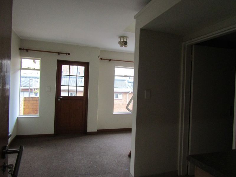 An empty living area featuring carpeted flooring, a timber-framed glass door, and neutral walls, offering a blank canvas for potential interior updates.