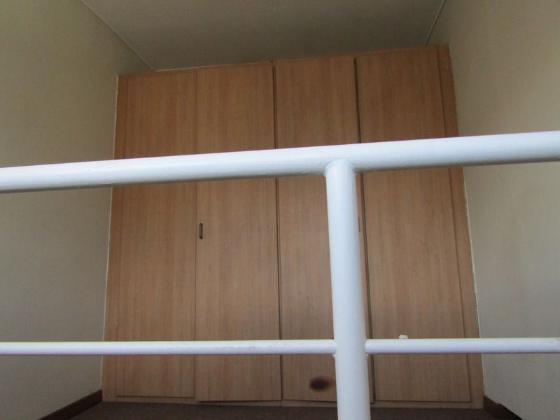A bedroom interior featuring built-in wooden cupboards and a white metal balustrade, showing signs of wear.