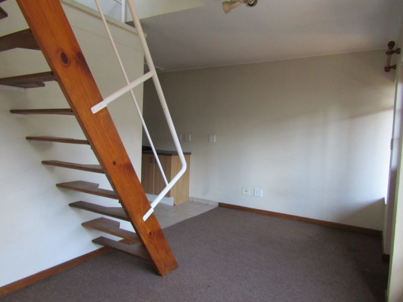 An empty open-plan living area featuring a wooden staircase with a metal handrail and a small kitchen corner with built-in cabinetry.