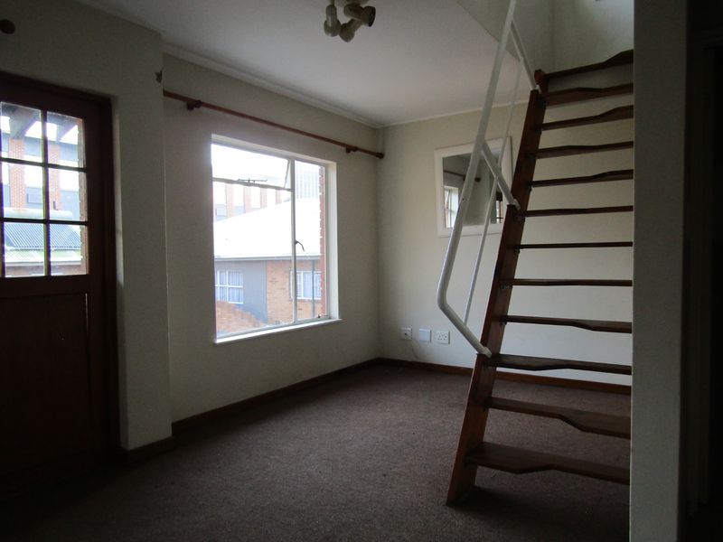 An empty living area featuring a wooden staircase with a metal handrail, large window, and timber-framed door, offering a blank canvas for renovation.