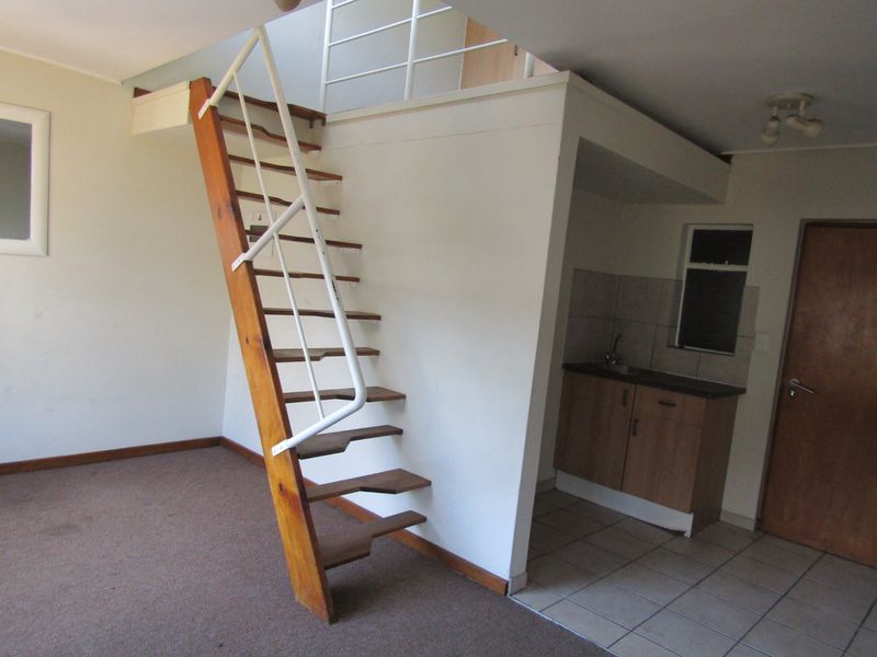 Open plan living area featuring a mezzanine level with a wooden staircase, kitchenette with built-in cabinetry, and a mix of carpet and tile flooring.
