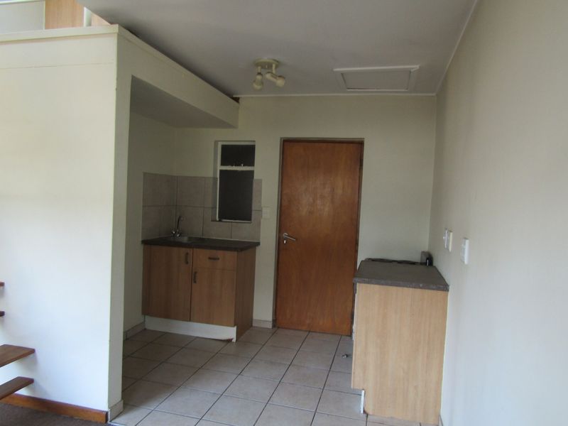 A compact, empty kitchen area featuring basic cabinetry, laminate countertops, a stainless steel sink, and tiled flooring, ready for modernization.