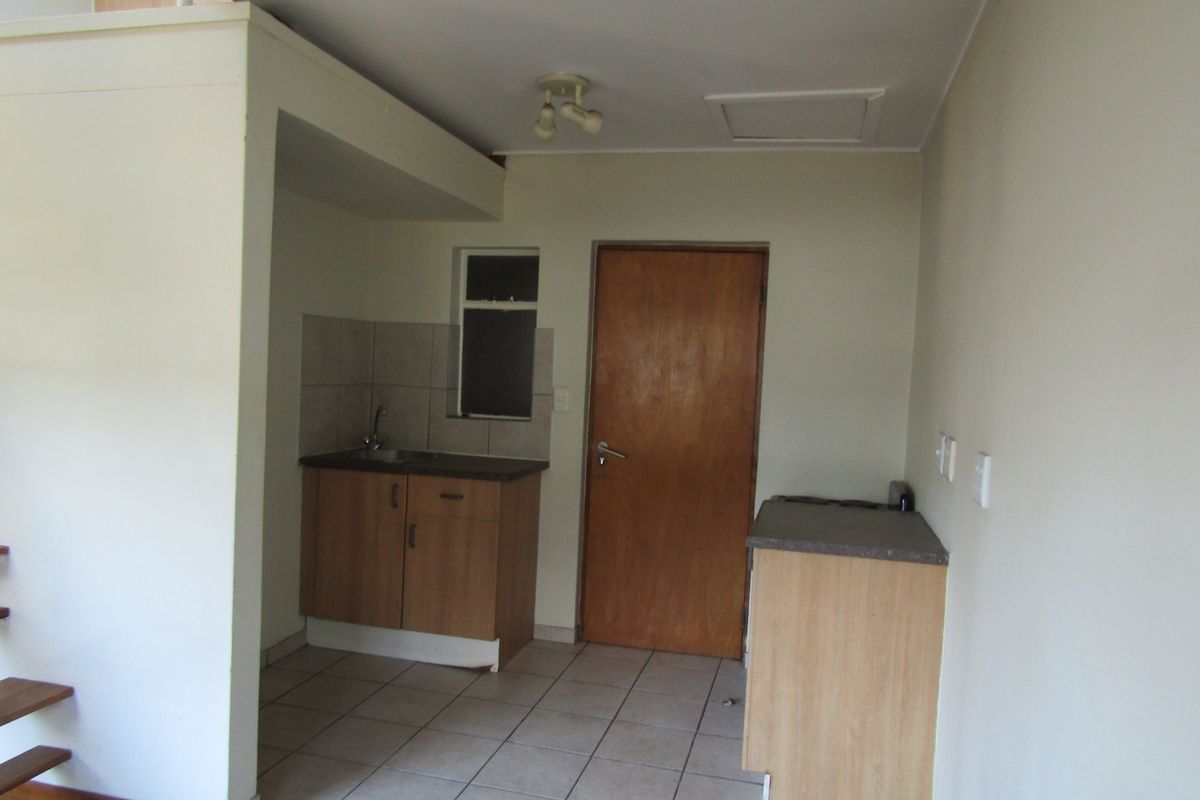 A compact, empty kitchen area featuring basic cabinetry, laminate countertops, a stainless steel sink, and tiled flooring, ready for modernization.