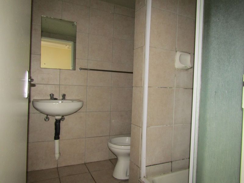 A dated bathroom featuring a wall-mounted basin, toilet, and shower enclosure with neutral wall and floor tiling.