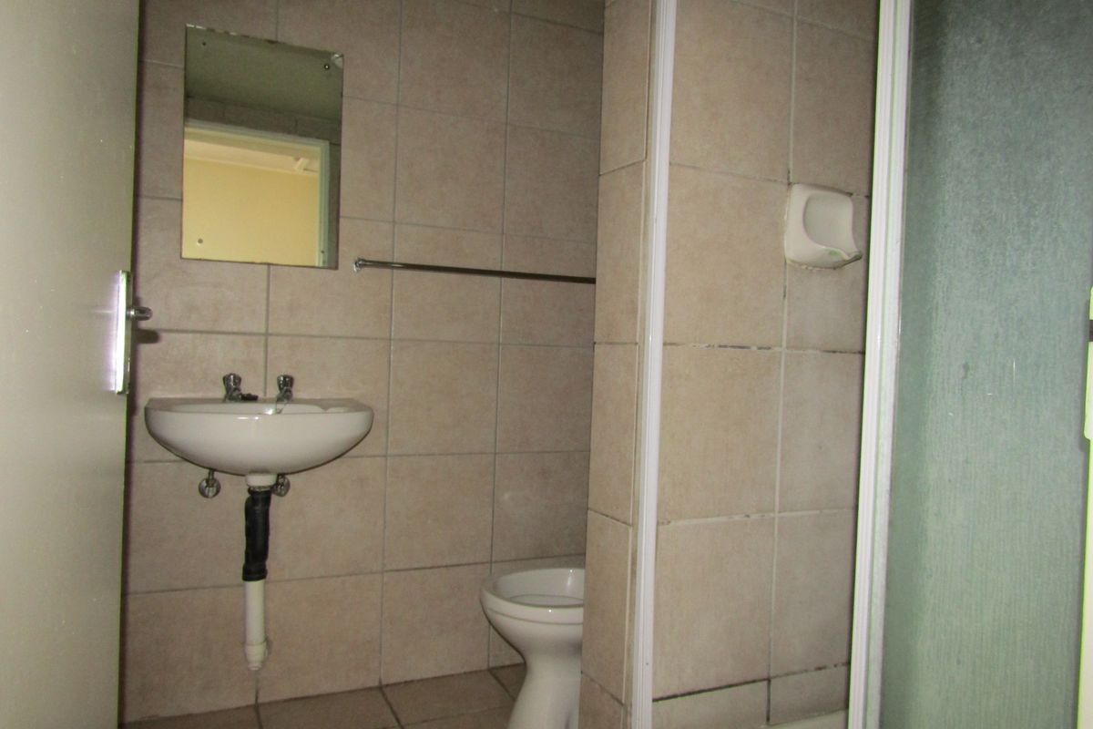 A dated bathroom featuring a wall-mounted basin, toilet, and shower enclosure with neutral wall and floor tiling.